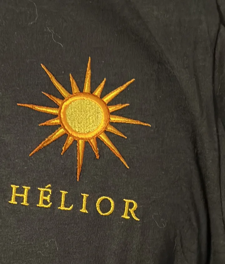 The embroidered chest logo, a golden sun above the name Hélior